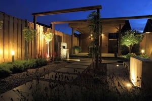 A photo of a landscaped backyard, surrounded by a fence with outdoor lighting.